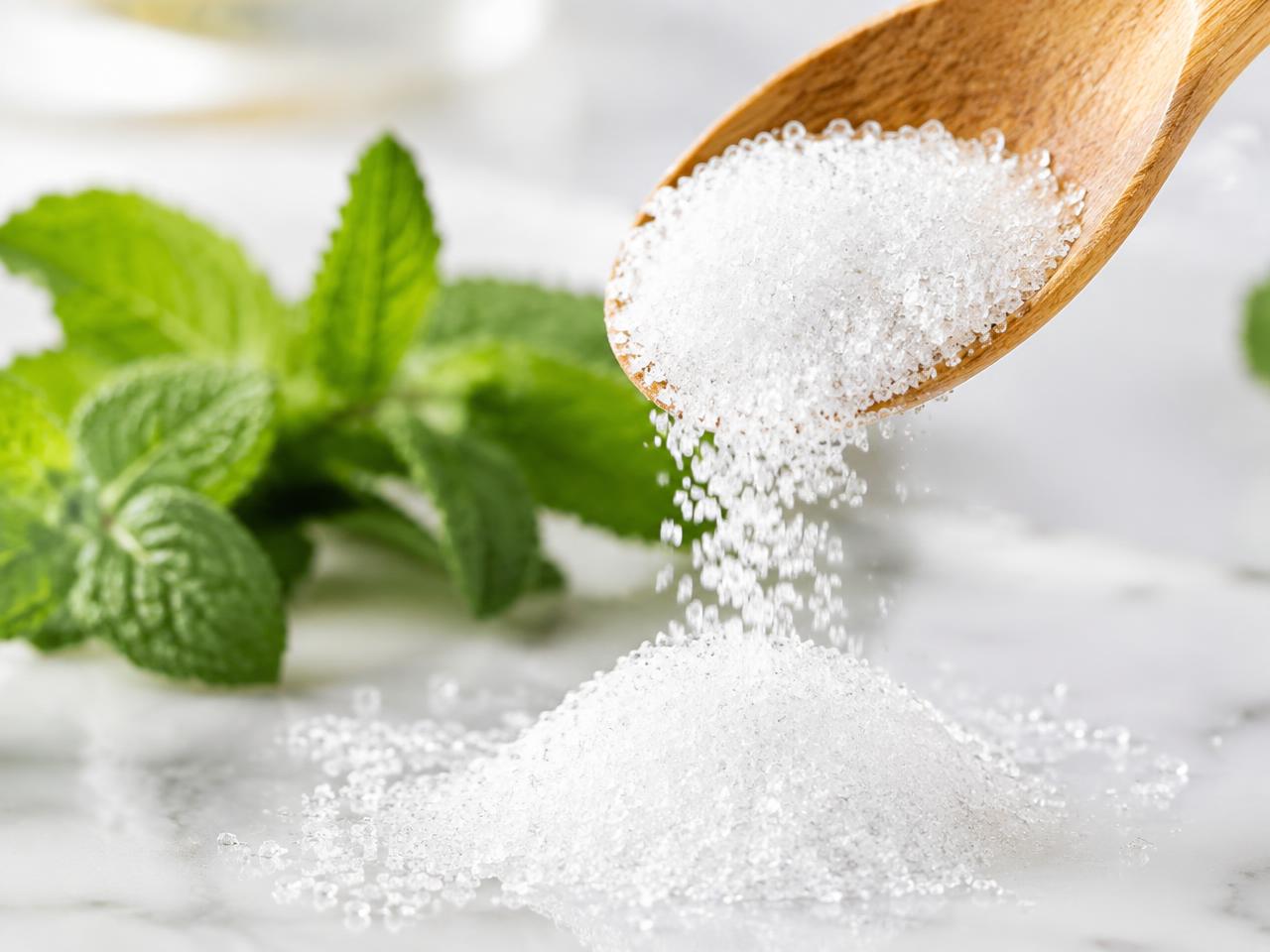 Erythritol crystals pouring from a wooden spoon